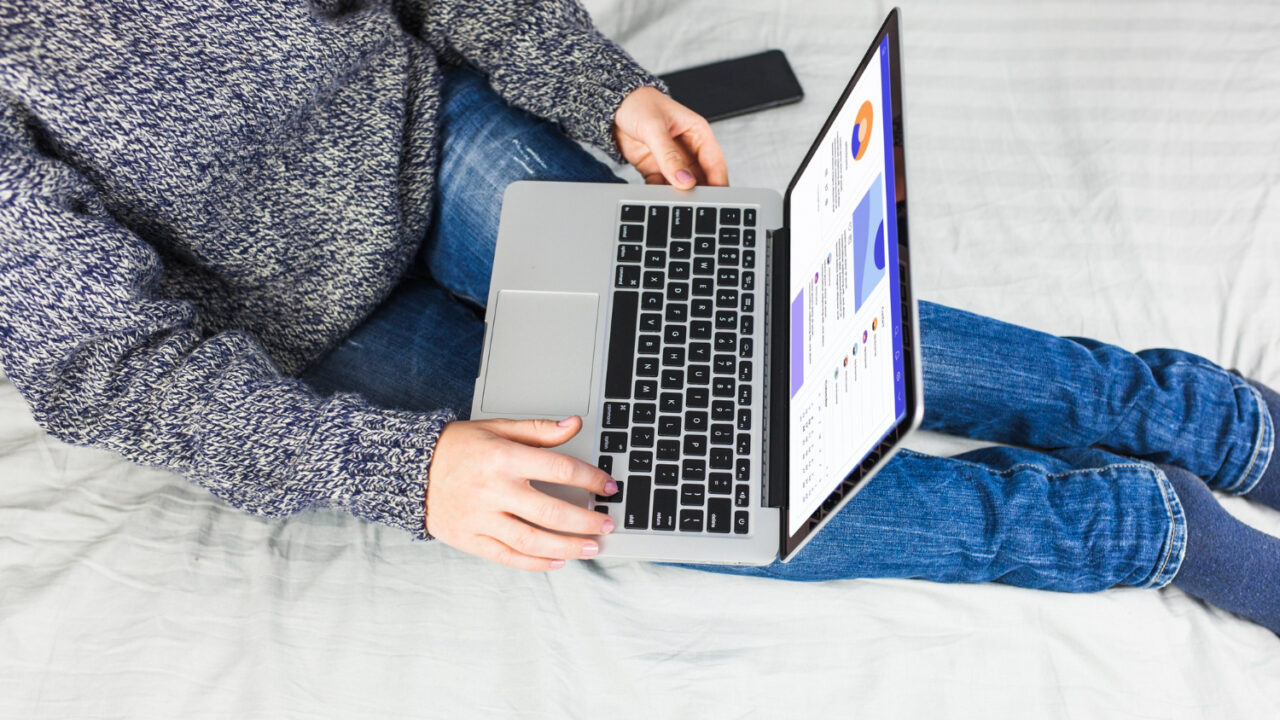 Seorang wanita duduk di atas tempat tidur dengan laptop.