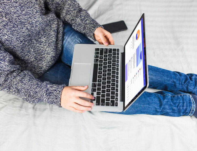 Seorang wanita duduk di atas tempat tidur dengan laptop.