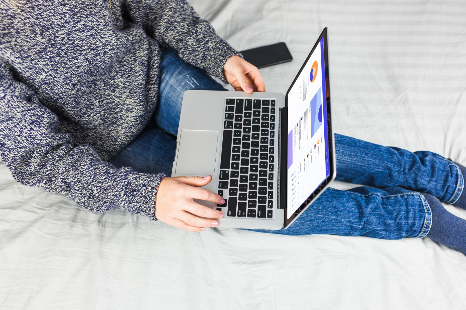 Seorang wanita duduk di atas tempat tidur dengan laptop.