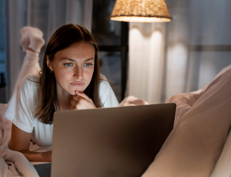 Seorang gadis sedang berbaring di tempat tidur dan melihat laptop.